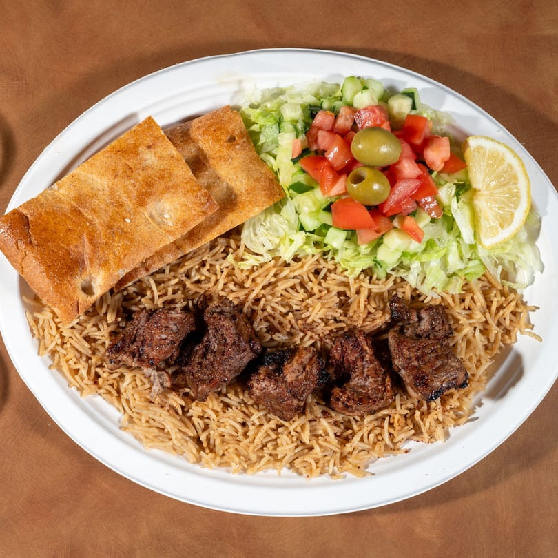 Zaytoon's Afghan lamb kebab with rice, salad, lemon, and flatbread on a white plate.