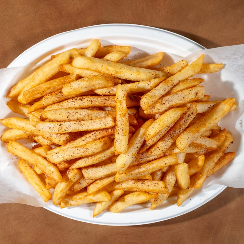 Golden Zaytoon french fries seasoned with spices, served in a white bowl with parchment paper.