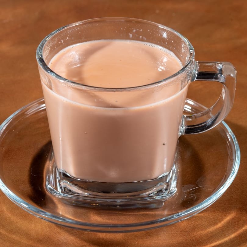 A clear glass mug filled with creamy Afghan chai tea sits on a matching saucer.